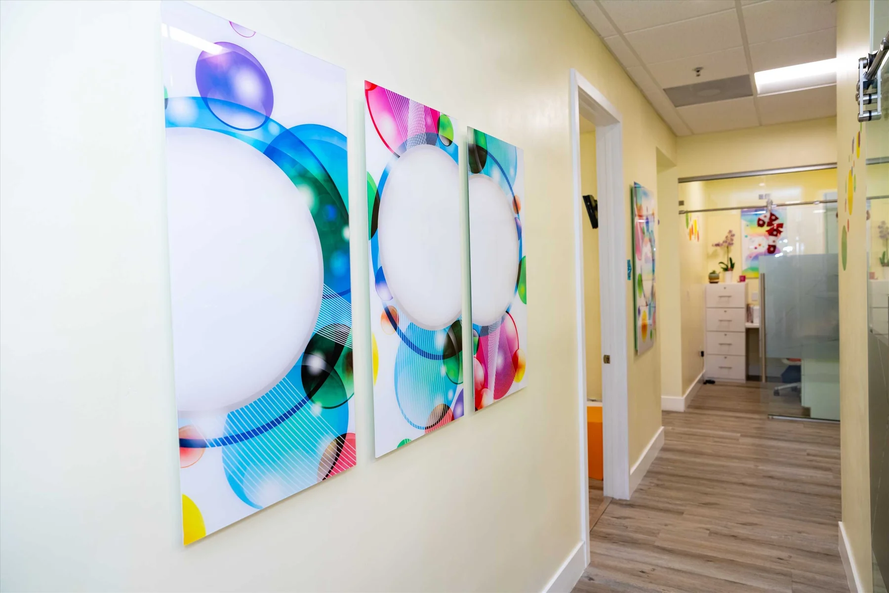 AC Pediatric Dentistry & Orthodontics — Corridor with a triptych of bubble panels, each with a large white circle, on a pale yellow wall