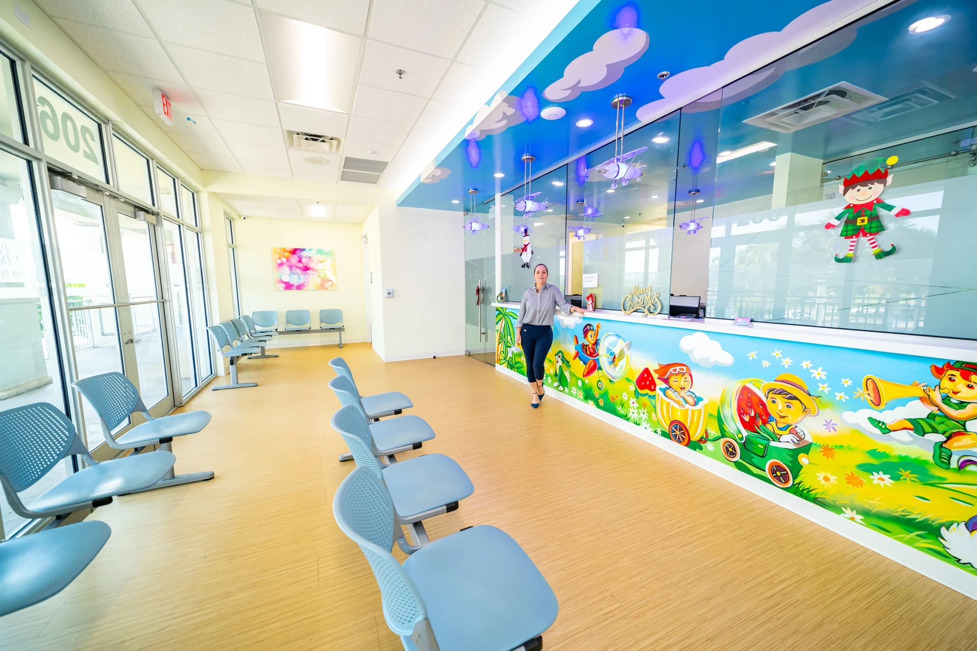 Pediatric Dentistry — Wide view of the waiting room with a person at the mural-painted counter under airplane-shaped lamps