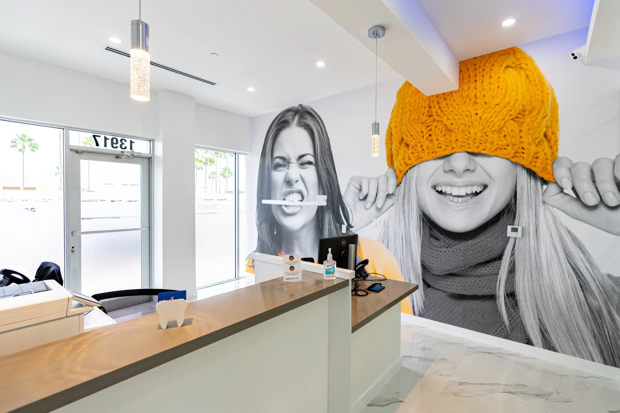 Anillo Dentistry — Reception desk in front of a black-and-white mural of two faces, one under a yellow knit hat