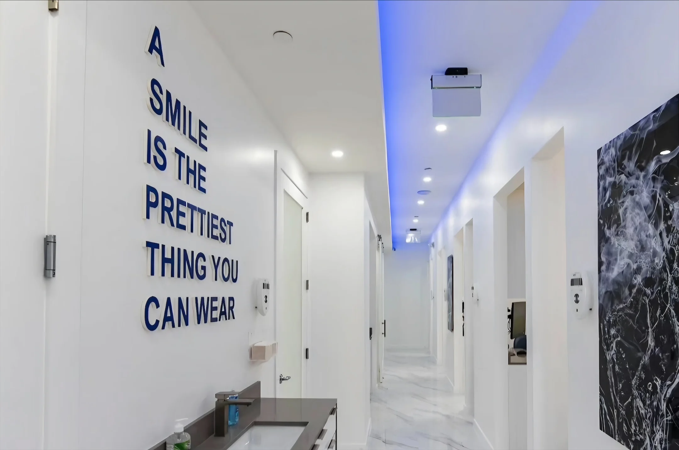 Anillo Dentistry — Corridor with A SMILE IS THE PRETTIEST THING YOU CAN WEAR in navy letters, beside a sink and a black-and-white water panel