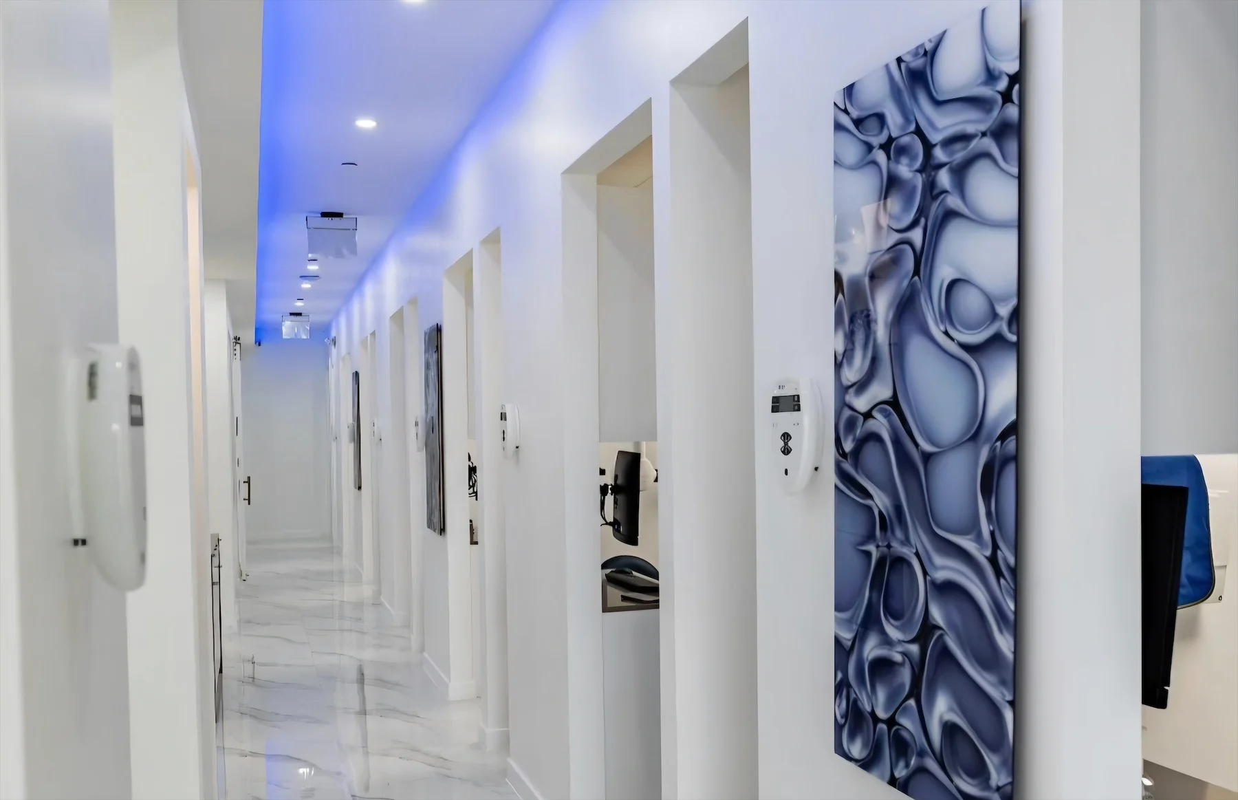 Anillo Dentistry — Corridor of treatment-room doorways under a blue cove light, with a large blue abstract panel in the foreground