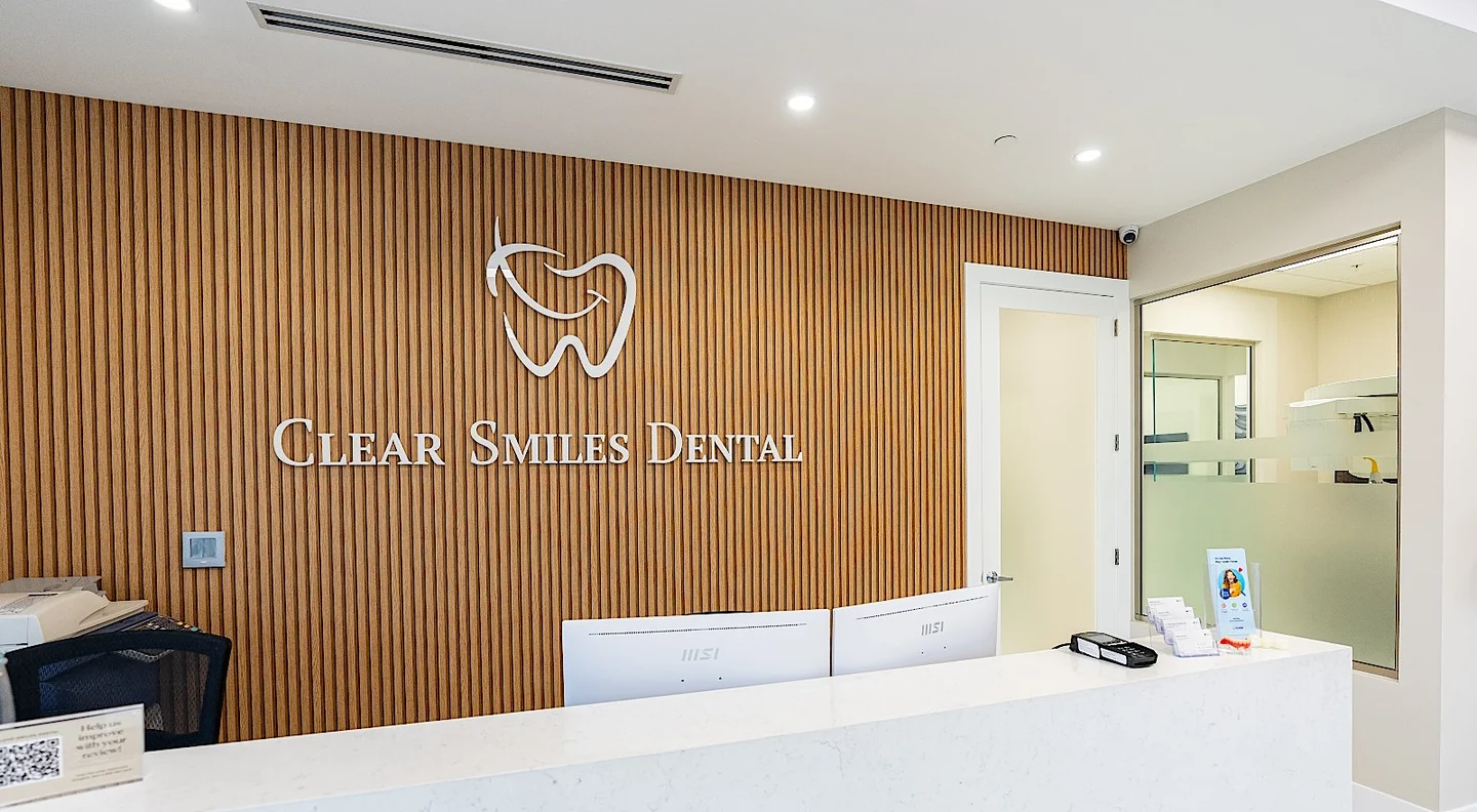 Clear Smiles Dental — Reception wall of vertical oak slats with the logo and name in white, behind a pale stone desk