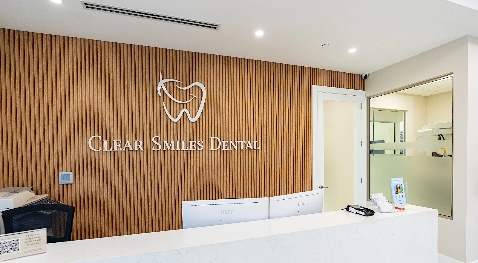 Clear Smiles Dental — Reception wall of vertical oak slats with the logo and name in white, behind a pale stone desk