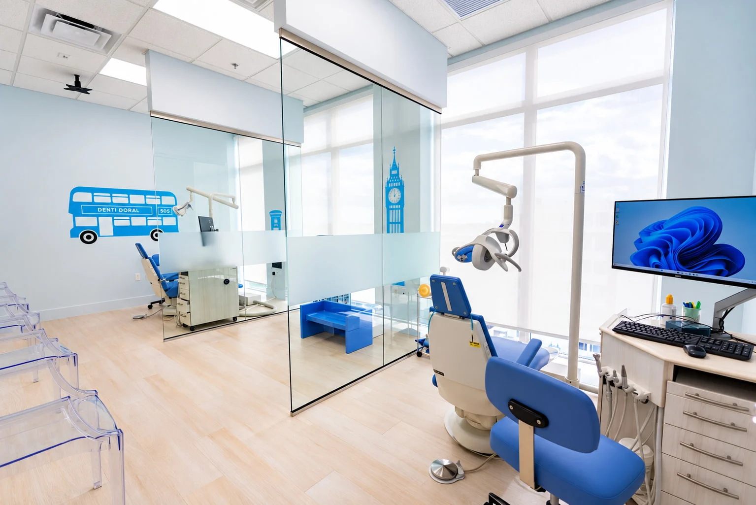 Denti Pediatric Dentistry — Open treatment area with blue dental chairs, glass partitions and double-decker bus and Big Ben decals