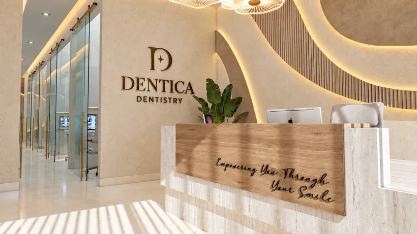 Dentica — Reception with the “Dentica Dentistry” logo and a wood desk lettered “Empowering You Through Your Smile”