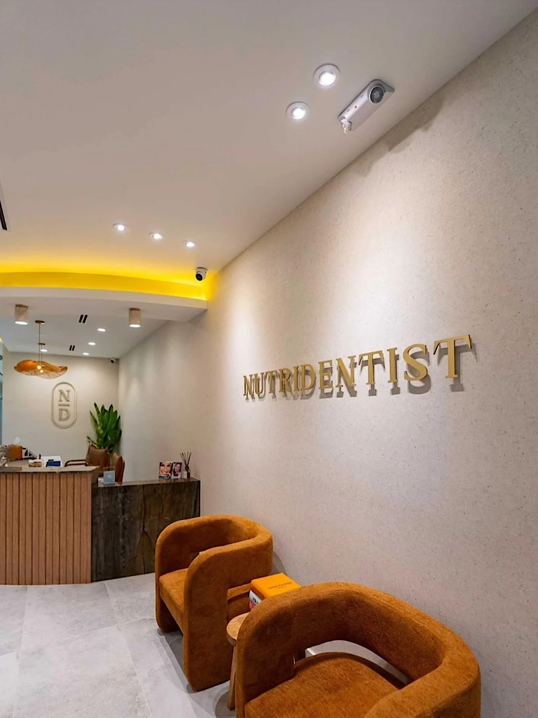 Nutridentist — Lobby with gold NUTRIDENTIST lettering on a textured wall, rust armchairs and a slatted wood reception desk