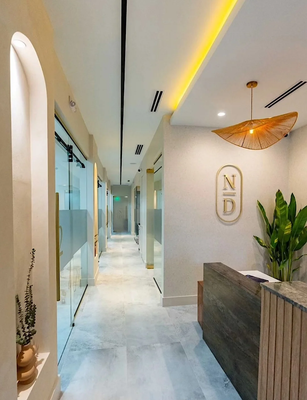 Nutridentist — Corridor past the reception desk, with arched niches, glass doors and the gold N/D monogram on the wall