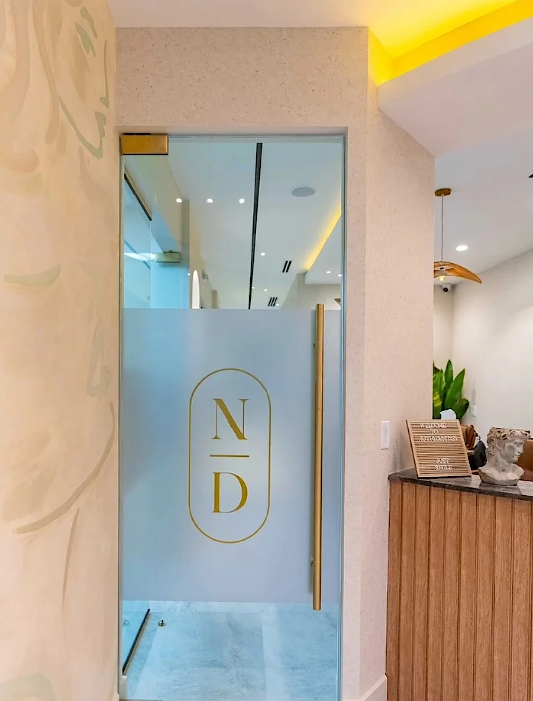 Nutridentist — Glass door with a frosted band and the gold N/D monogram, beside the reception desk