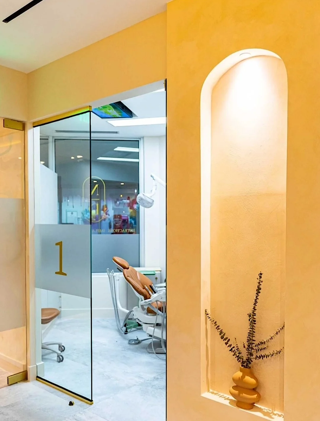 Nutridentist — Glass door marked 1 opening onto a treatment room, next to a lit arched niche with a dried branch