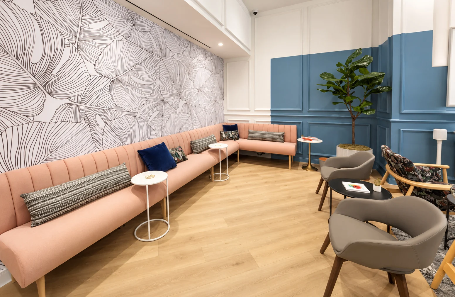 One Medical — Long peach banquette under a wall of oversized line-drawn leaves, with blue paneling and gray armchairs
