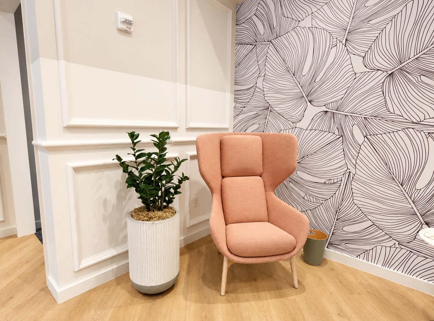 One Medical — Peach wing chair and a potted plant where white wall paneling meets the leaf-drawn wallpaper