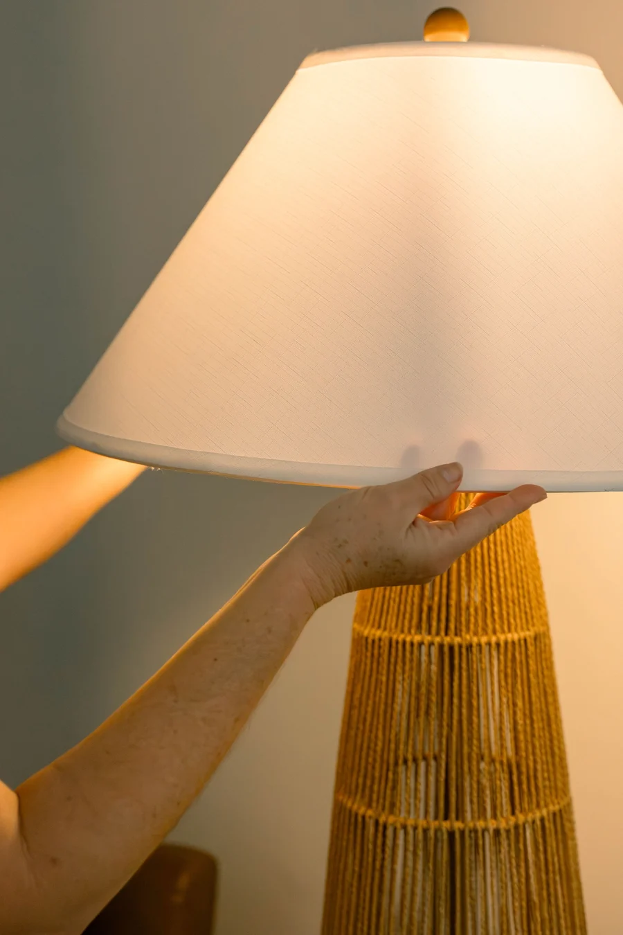 A hand adjusting the shade of a rattan floor lamp
