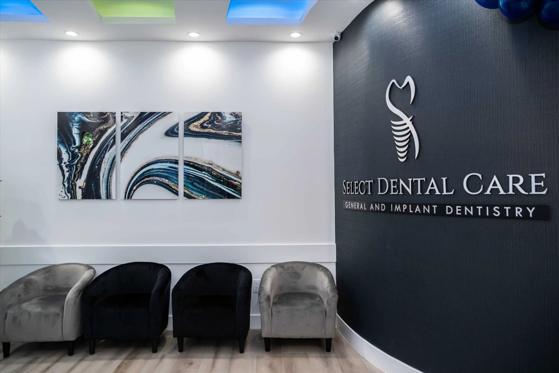 Select Dental Care — Reception with the practice name on a dark wall, an agate triptych and gray and black velvet chairs