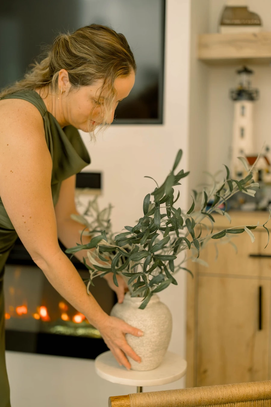 Yai Gómez placing a vase of olive branches on a side table in a finished living room